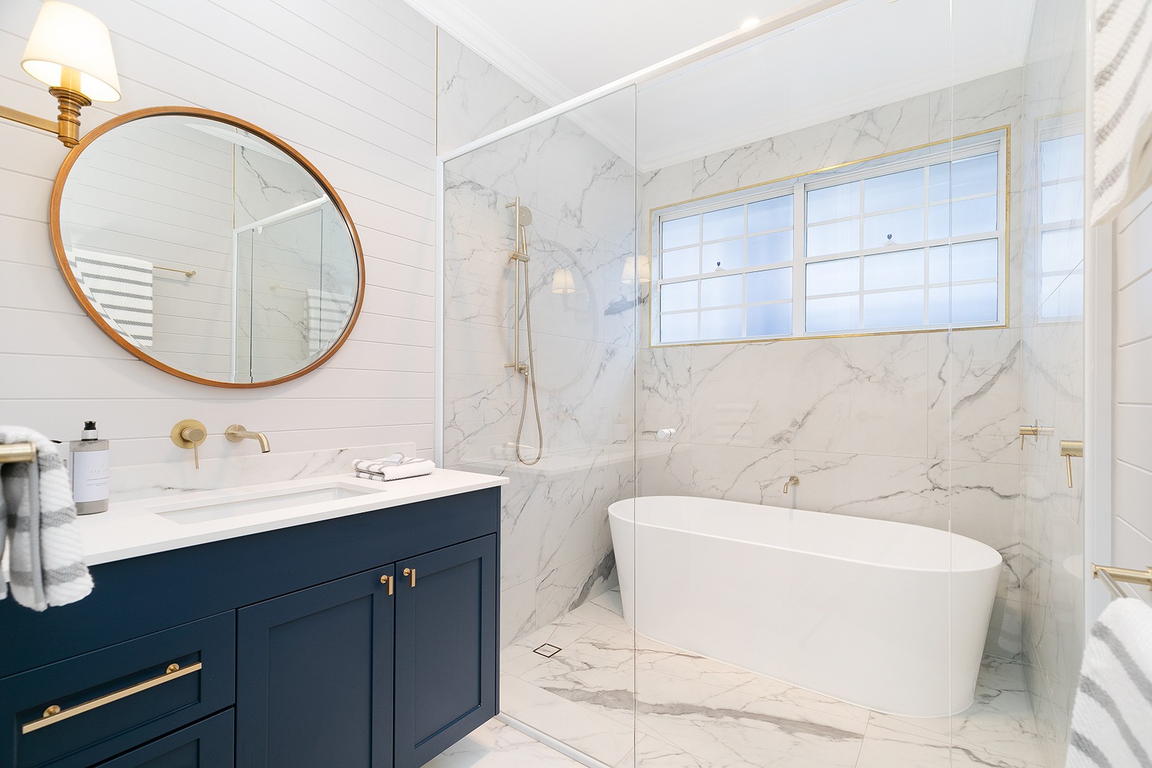 A bathroom with a navy blue vanity and a free standing bath in the glass enclosed shower