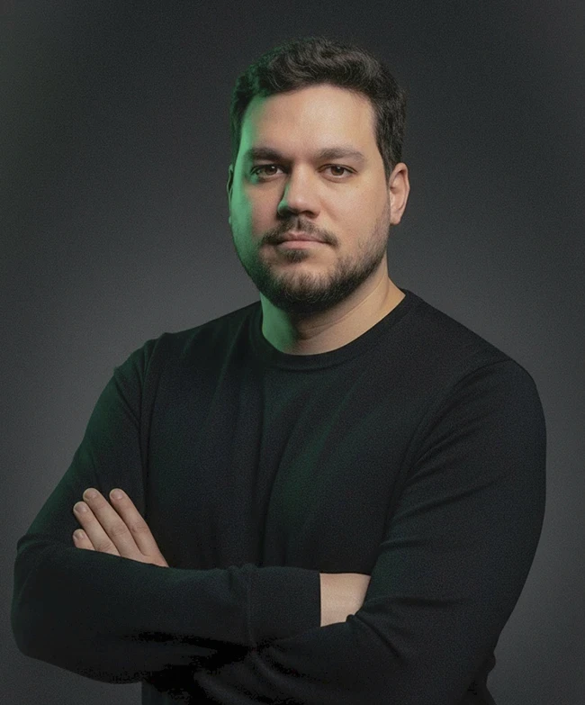 Portrait of a young man with short hair, wearing a dark t-shirt, against a plain background.