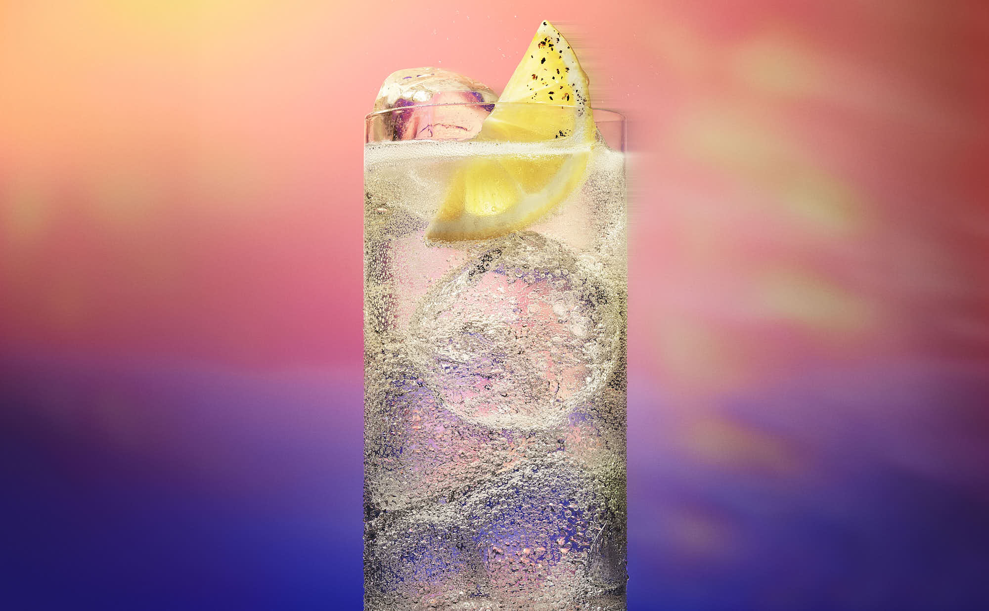 A colorful cocktail in a tall glass, topped with lemon wedge, against a soft gradient background.