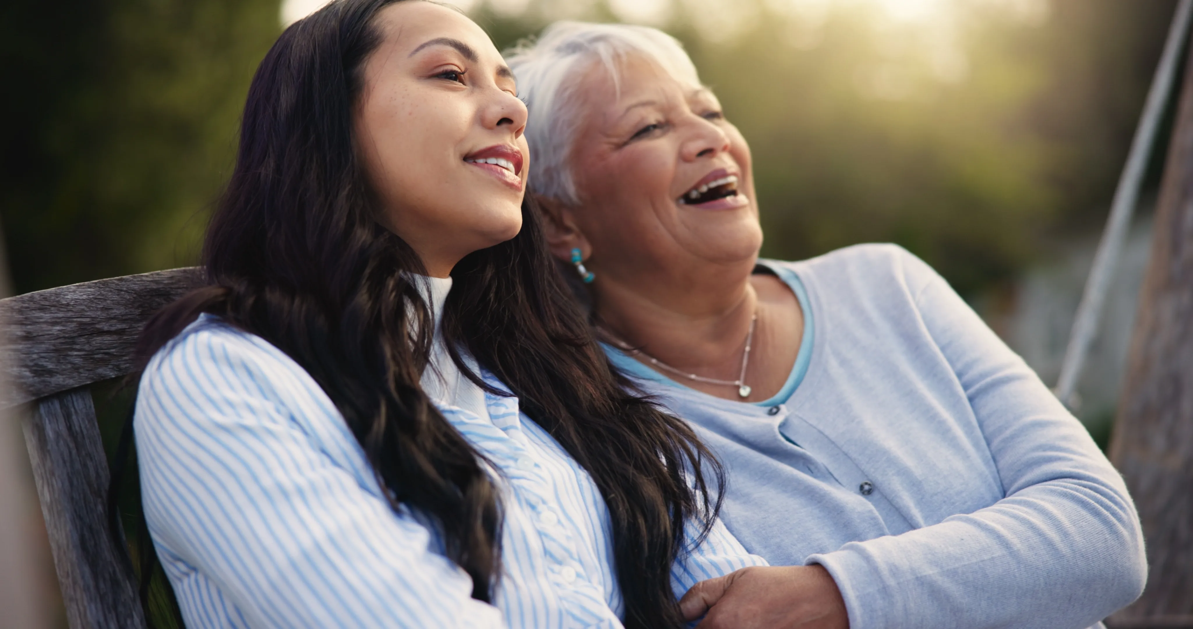 A heartwarming photo of a young woman smiling and embracing an elderly woman outdoors, capturing a moment of care and connection.