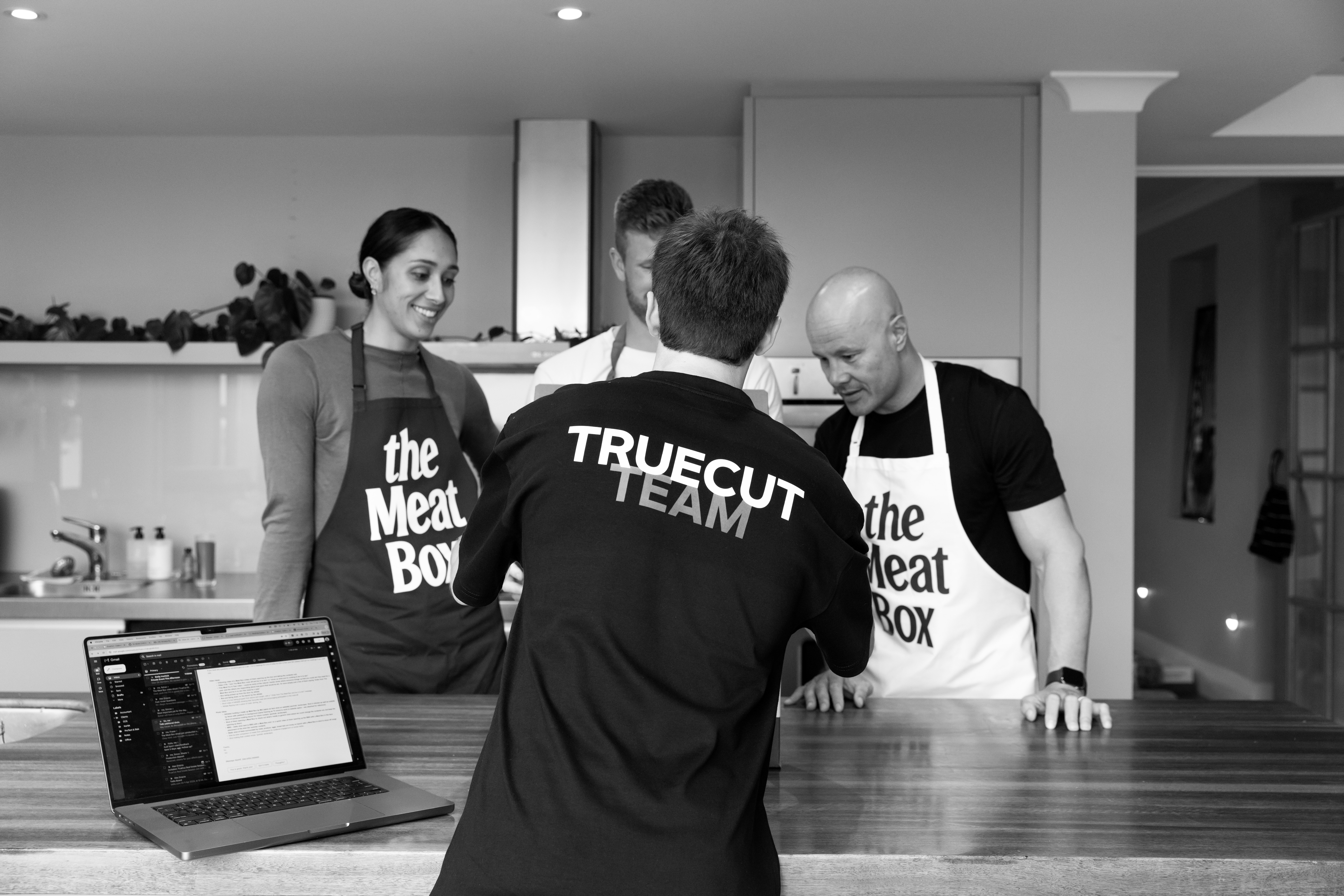 Black and white image of people working at a table with laptops, showing hands gesturing during discussion of digital content displayed on screens, with fabrica® logo in the corner.
