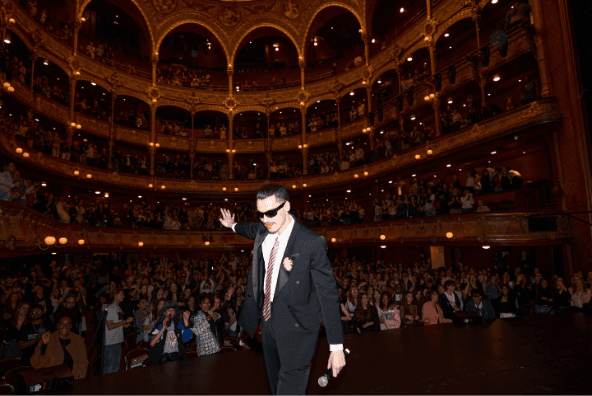 A person in a suit and tie on a stage with a microphone

AI-generated content may be incorrect.