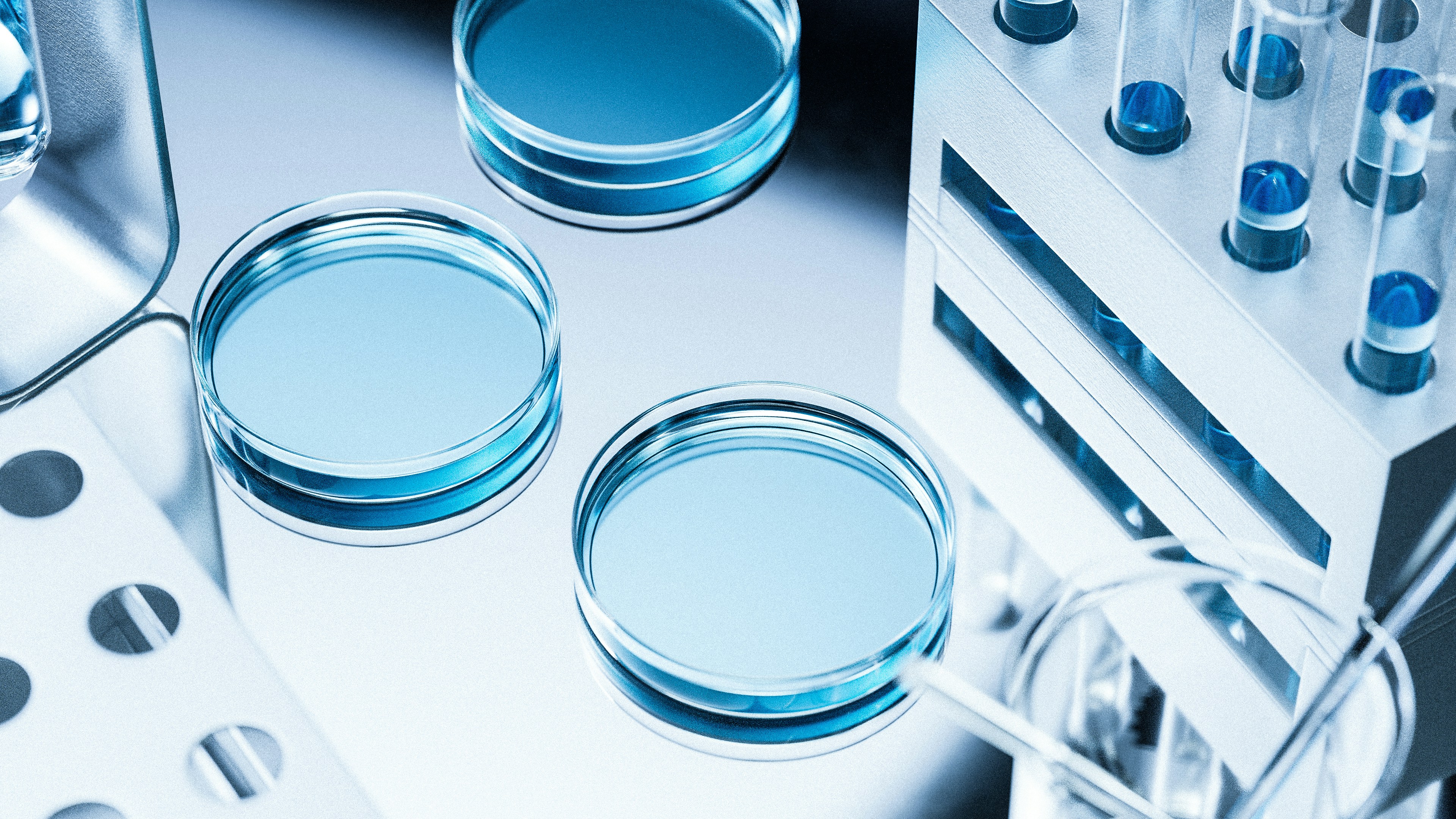 Close-up of three blue-tinted petri dishes and a rack of capped test tubes with blue liquid on a stainless steel laboratory surface, representing analytical research and quality testing.