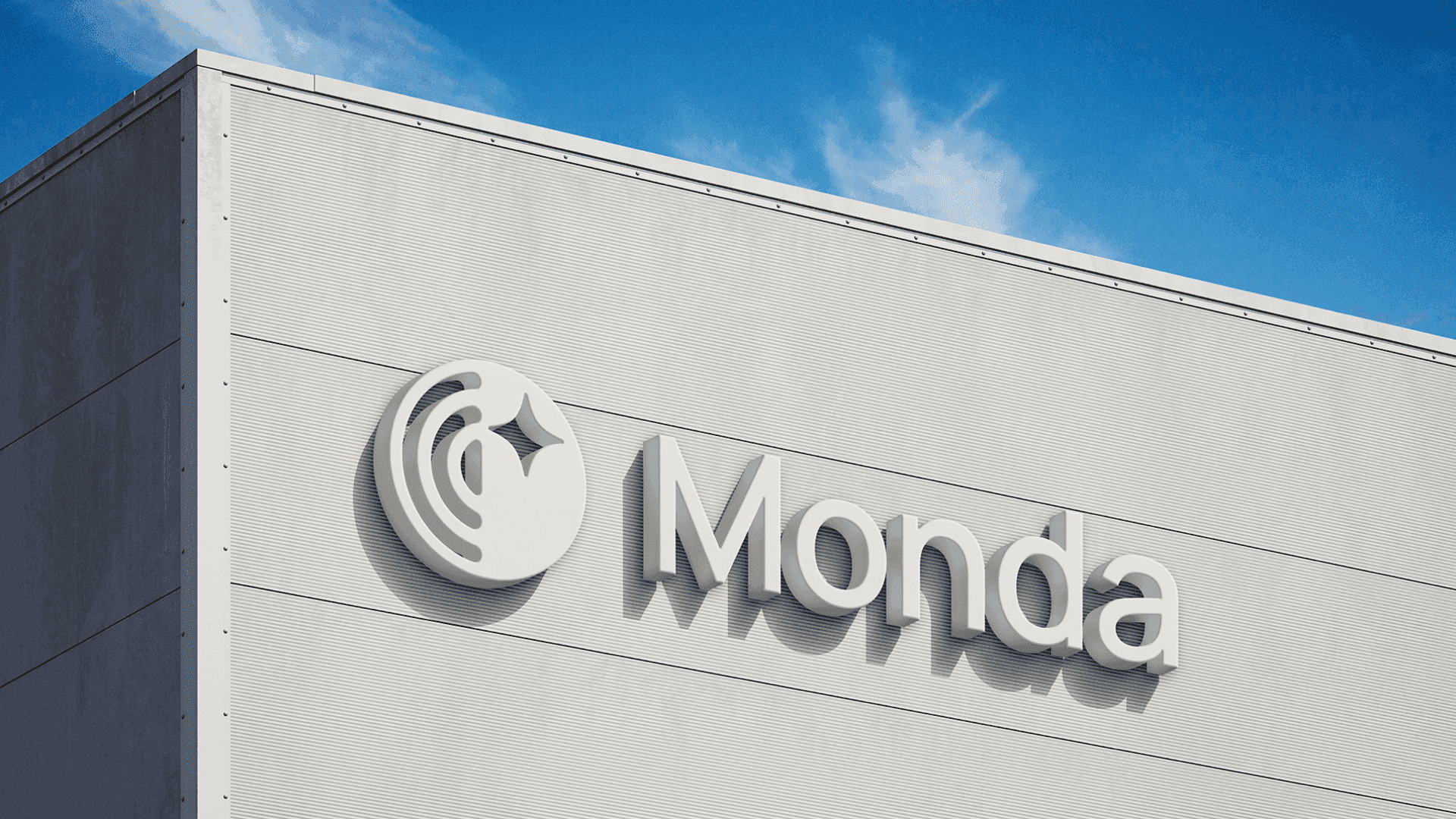 Dimensional Monda logo and lettering mounted on a grey corrugated building facade against blue sky
