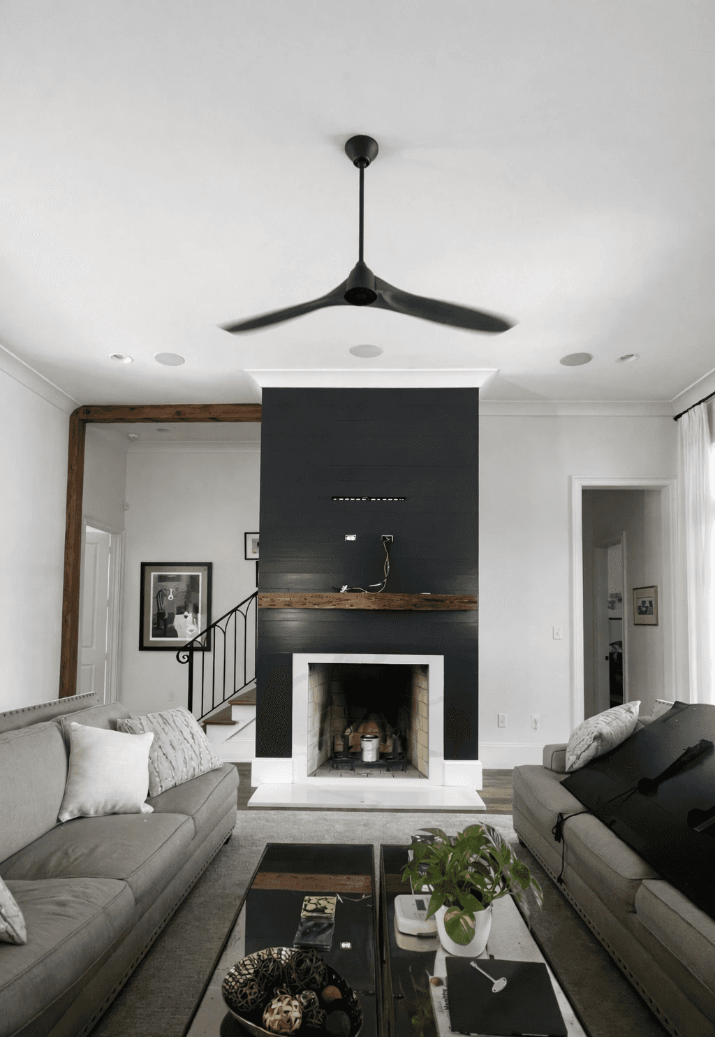 A modern, luxury beachfront villa with large glass windows and balconies overlooks a rocky shoreline, surrounded by palm trees at sunset.