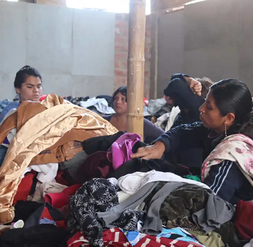 Personas en un local comunal seleccionando ropa de abrigo y frazadas provenientes de donaciones en Lima.