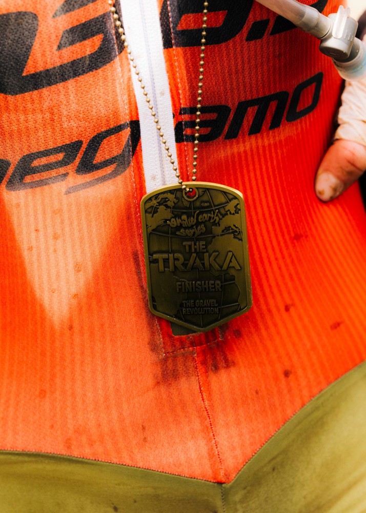 Close-up of The Traka finisher medal hanging over an orange cycling jersey