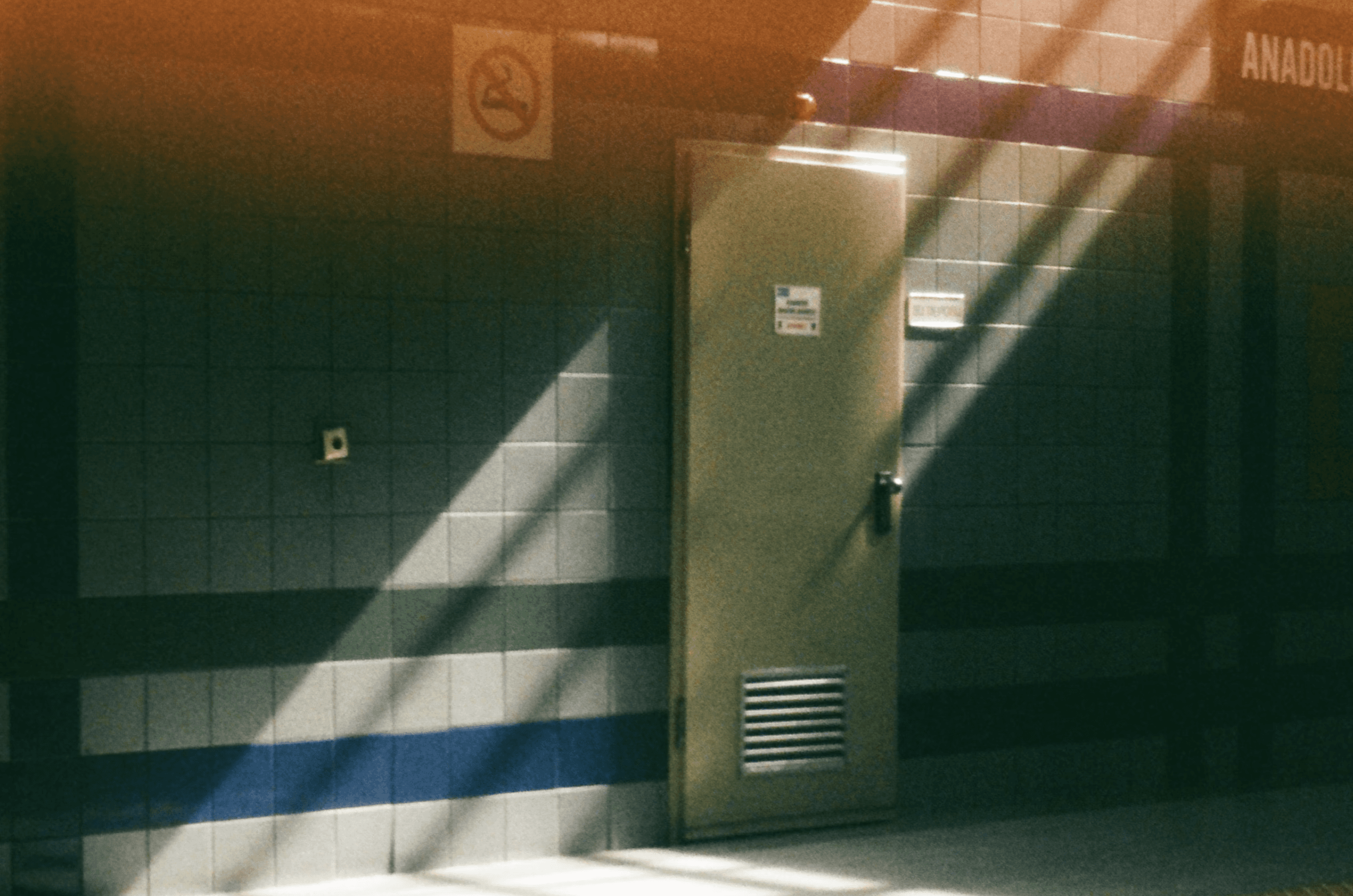 Empty subway station wall with tiled surface, closed utility door, and dramatic diagonal light and shadow patterns