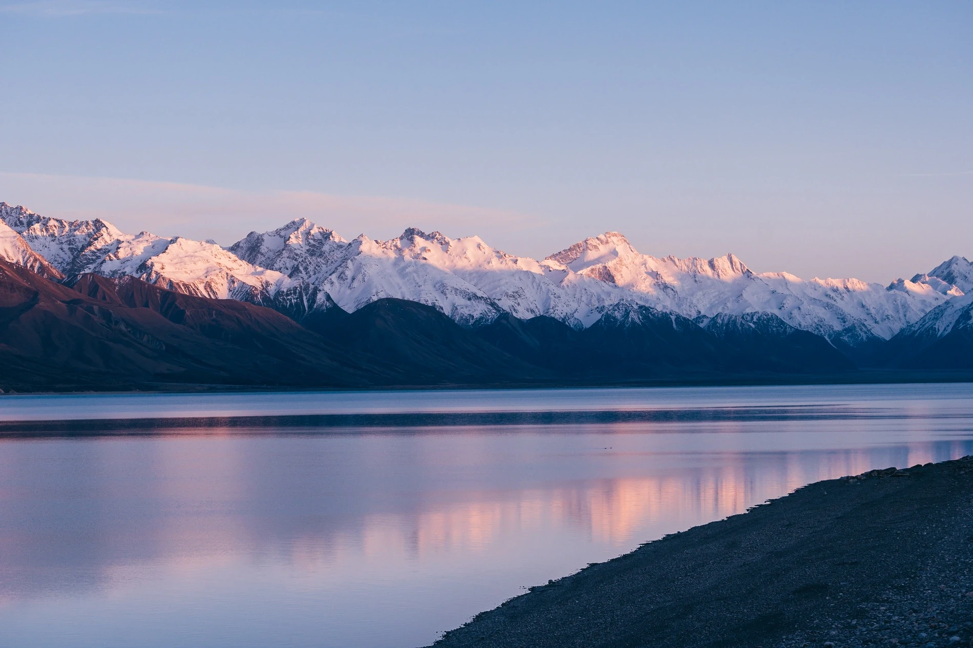 Pink dawn light on a distant snow range reflected in a glassy lake