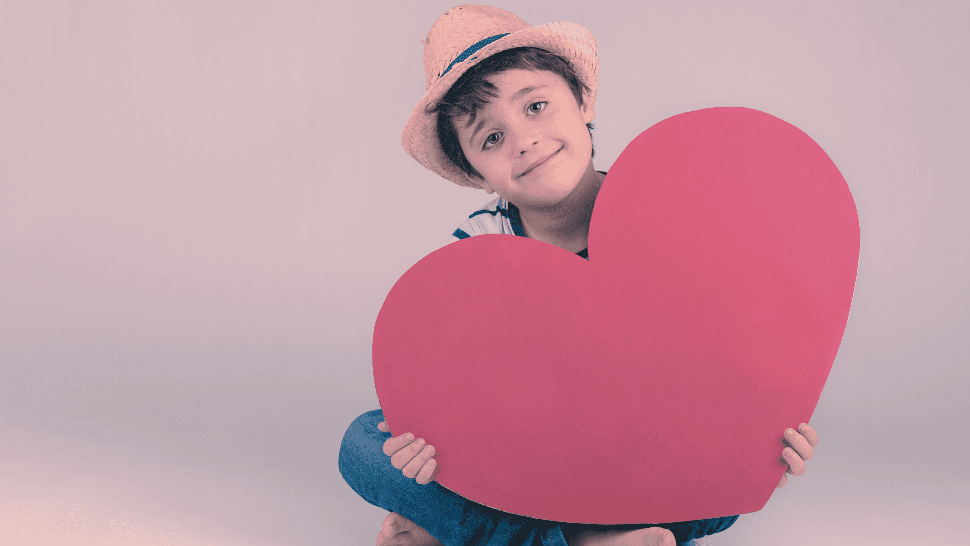 A young boy sat on the floor holding a big red love heart.