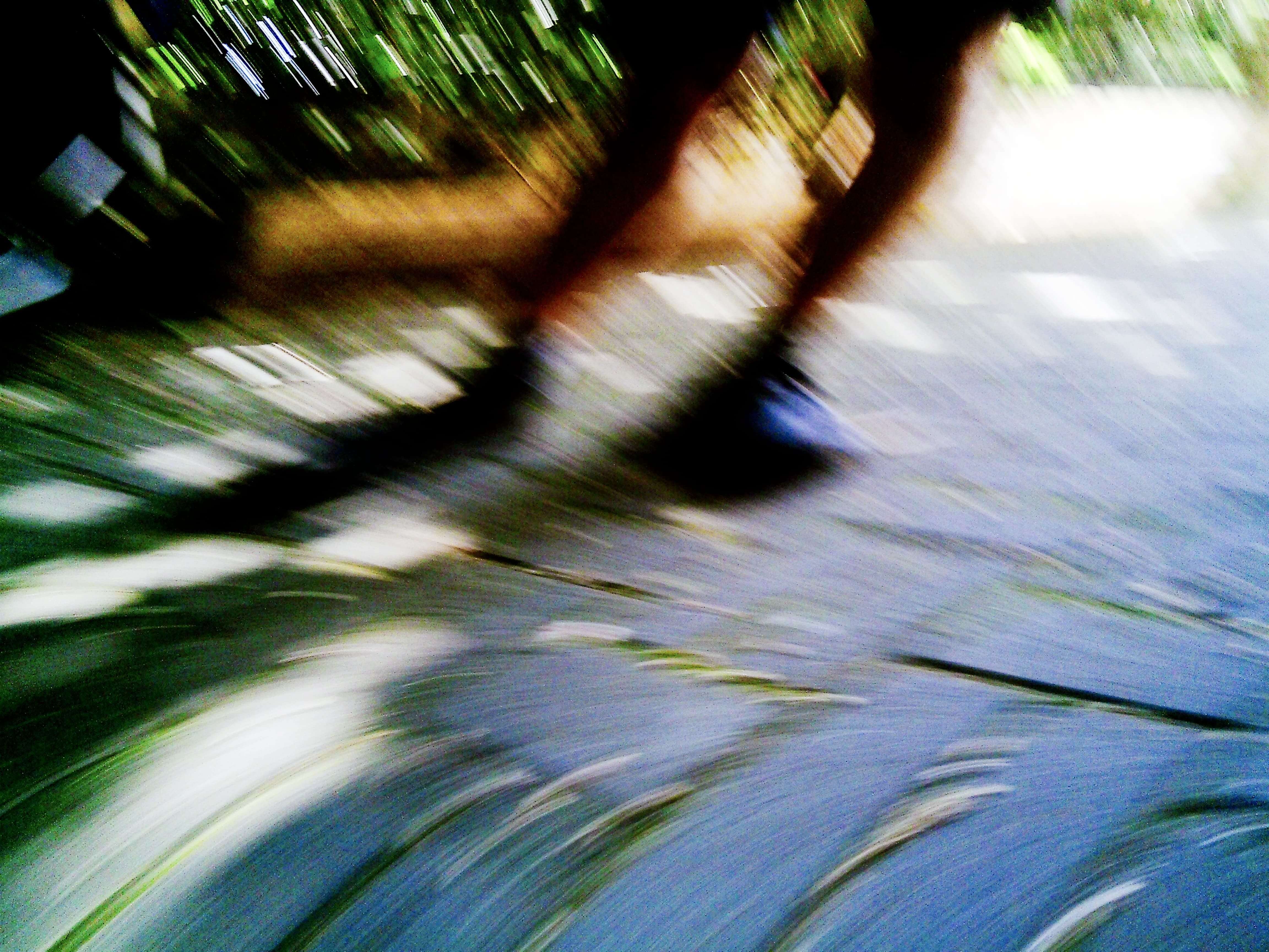 Diagonal motion blur transforms pedestrian and foliage into streaked bands of green, brown and blue