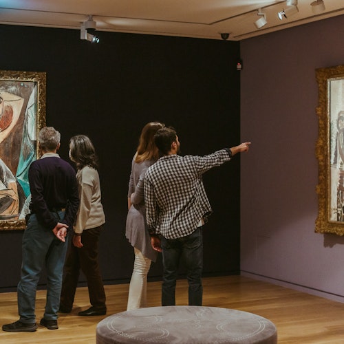 一群人在美术馆中，在柔和的聚光灯下欣赏墙上装裱好的画作。