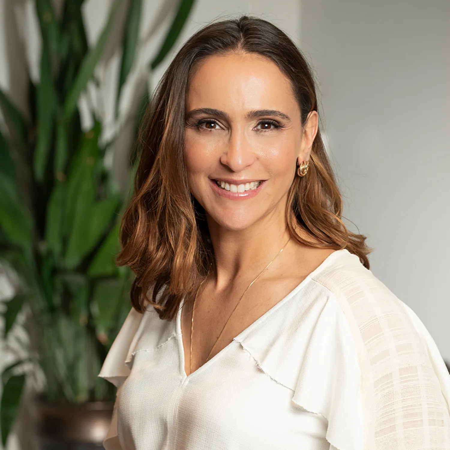 A young person with curly hair smiles at the camera while sitting in front of a laptop against a dark background.