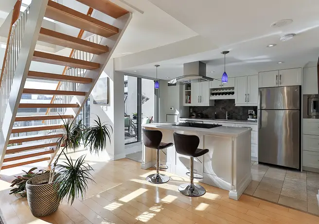 Modern interior featuring a wooden staircase with black railings, a wooden dining table with upholstered chairs, hardwood flooring, and natural light from a window.