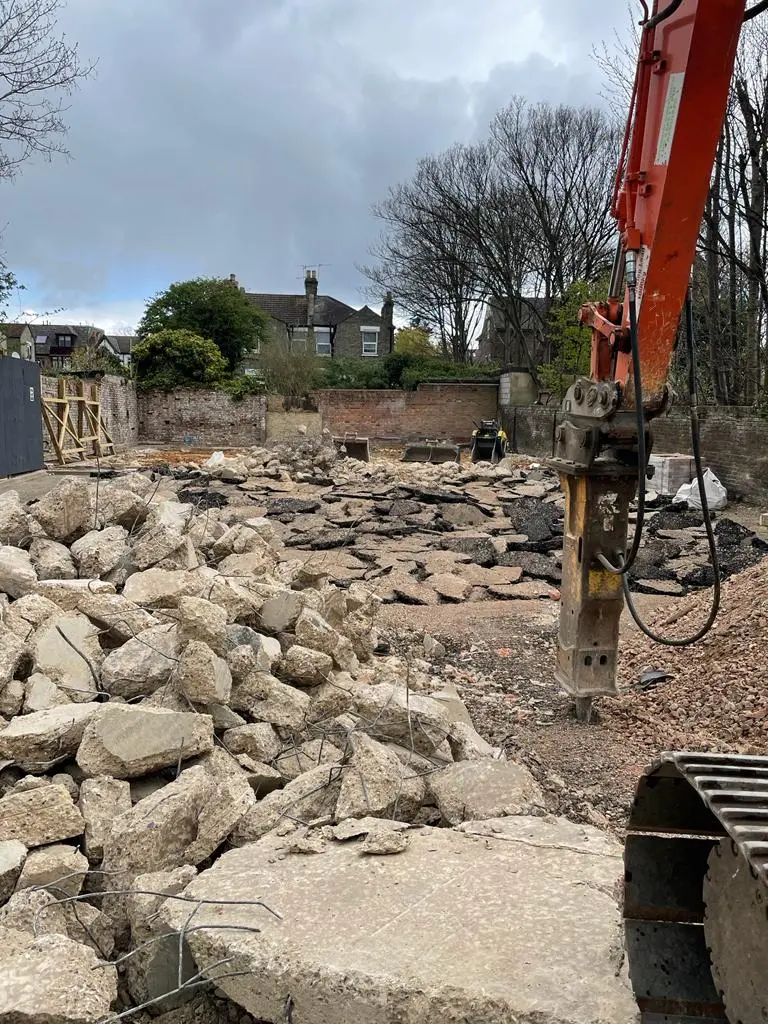 Construction site with a pile of stones and a machine working in the background under a cloudy sky.