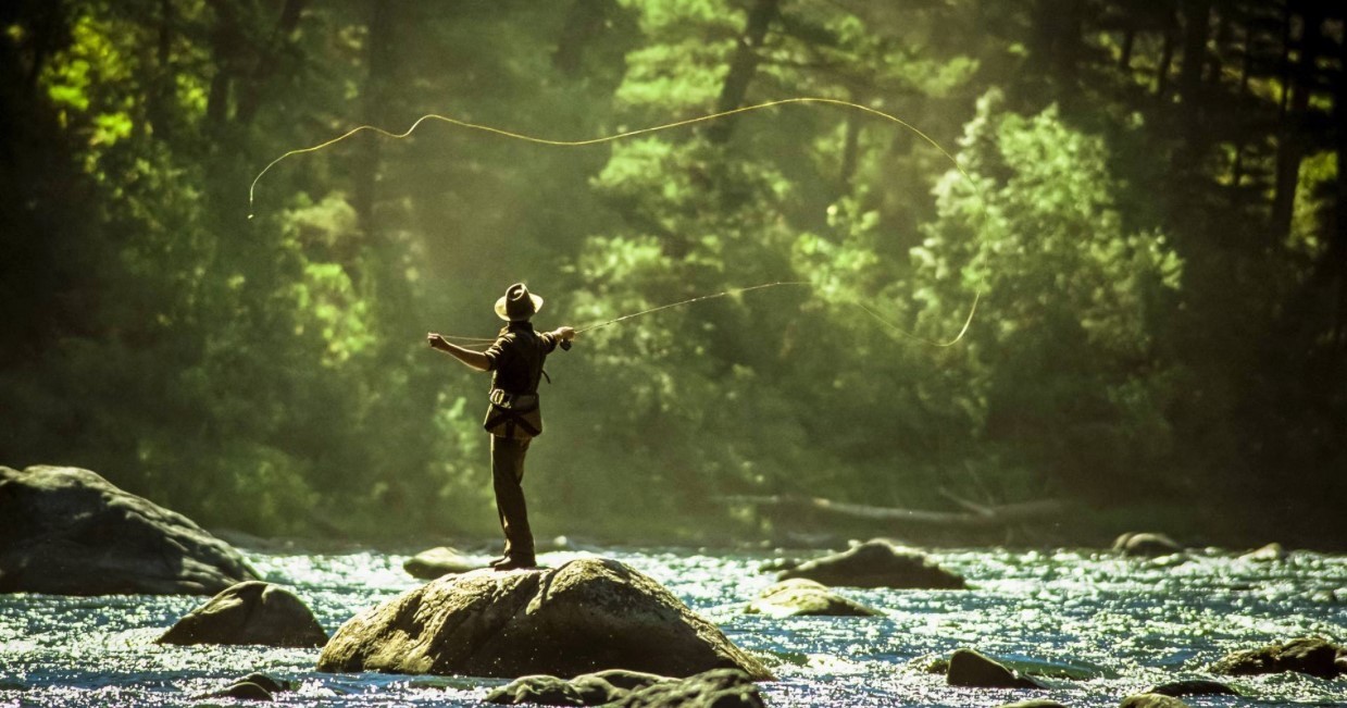 man standing on a rock casting a fly fishing rod into a river