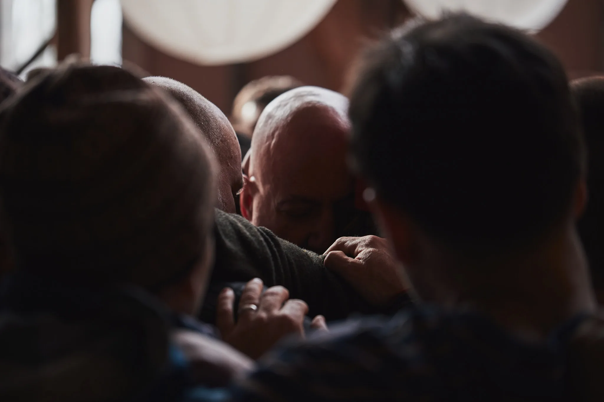men gripping shoulders in tight huddle — lifestyle photography by Tom Kubik