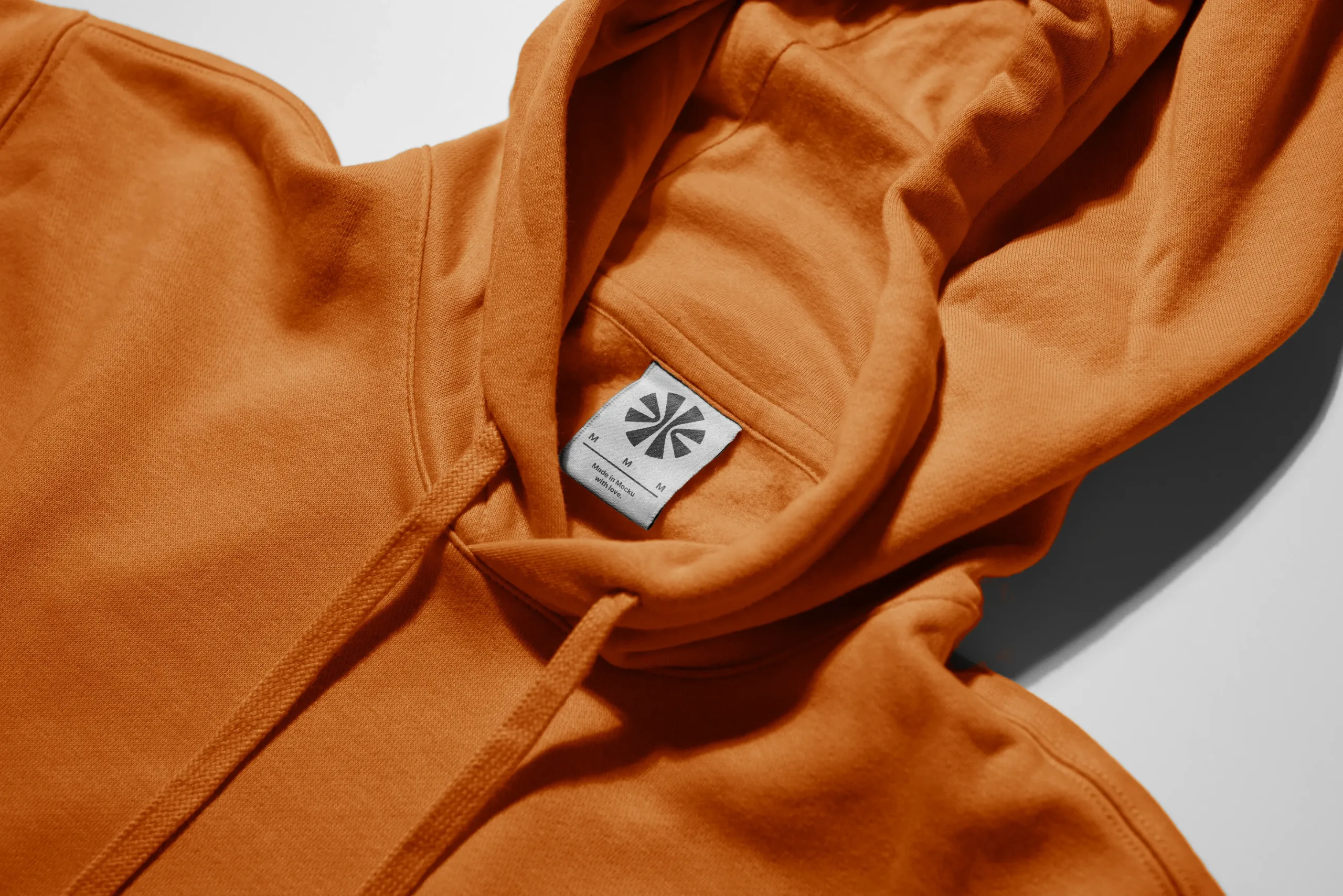 Mockup of an orange hoodie with a close-up view of the neckline and hood. The garment tag is clearly visible, set against a smooth fabric texture, ideal for showcasing branding or apparel design details.