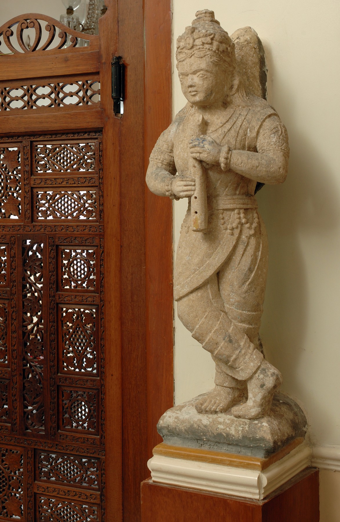 Stone angel sculpture positioned beside intricately carved wooden partition panel in a heritage interior.
