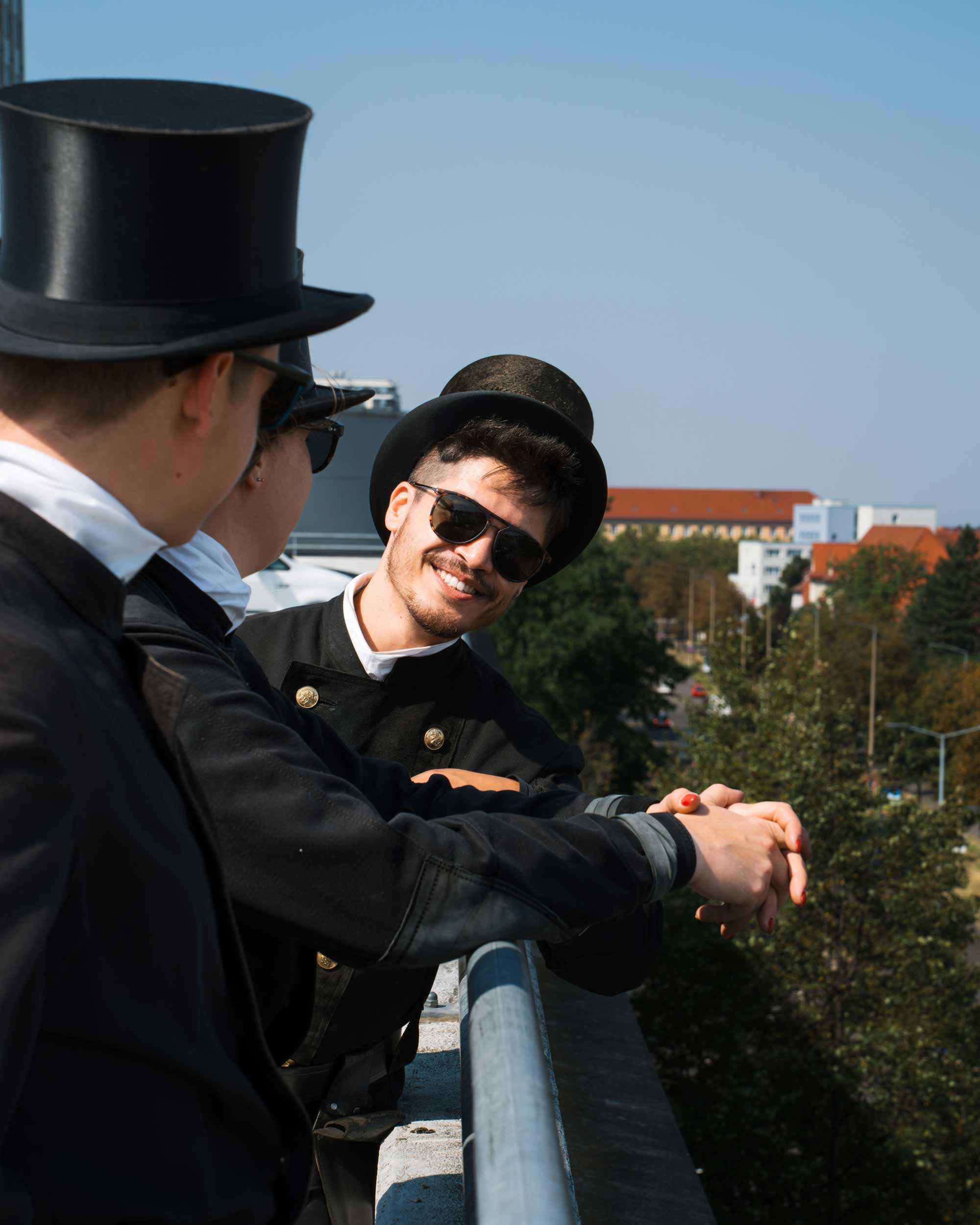 Three people in top hats smile and chat on a sunny rooftop, embodying storytelling for Zentralverband-Deutscher-Schornsteinfeger