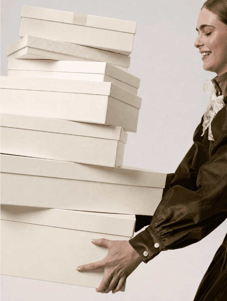An individual carrying a tall stack of light-coloured product and gift boxes.