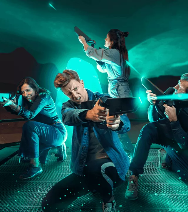 A team of four players actively firing VR weapons into the distance, immersed in a teal-lit sci-fi planetary environment.