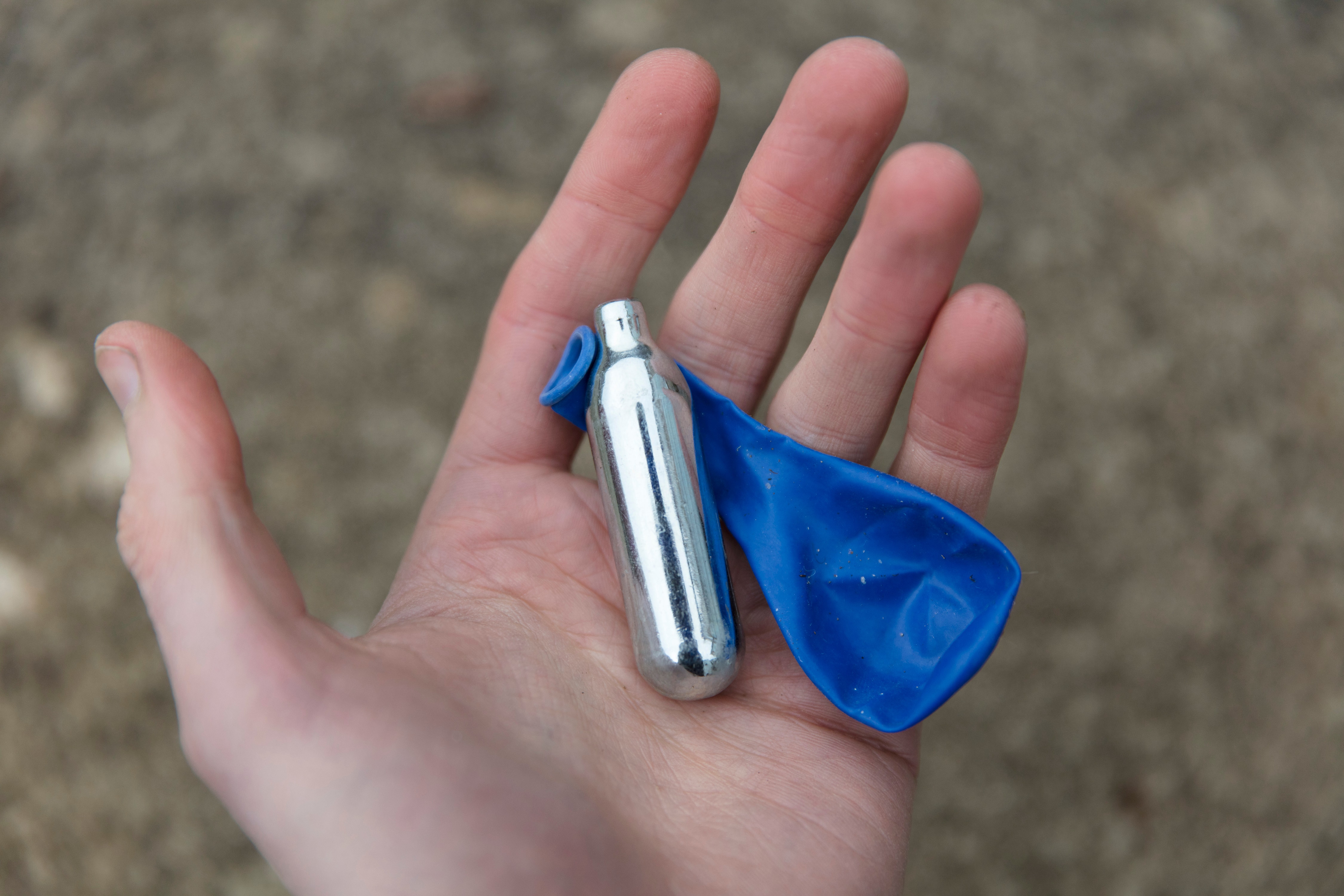 A hand holding a small metal canister and a deflated blue balloon.