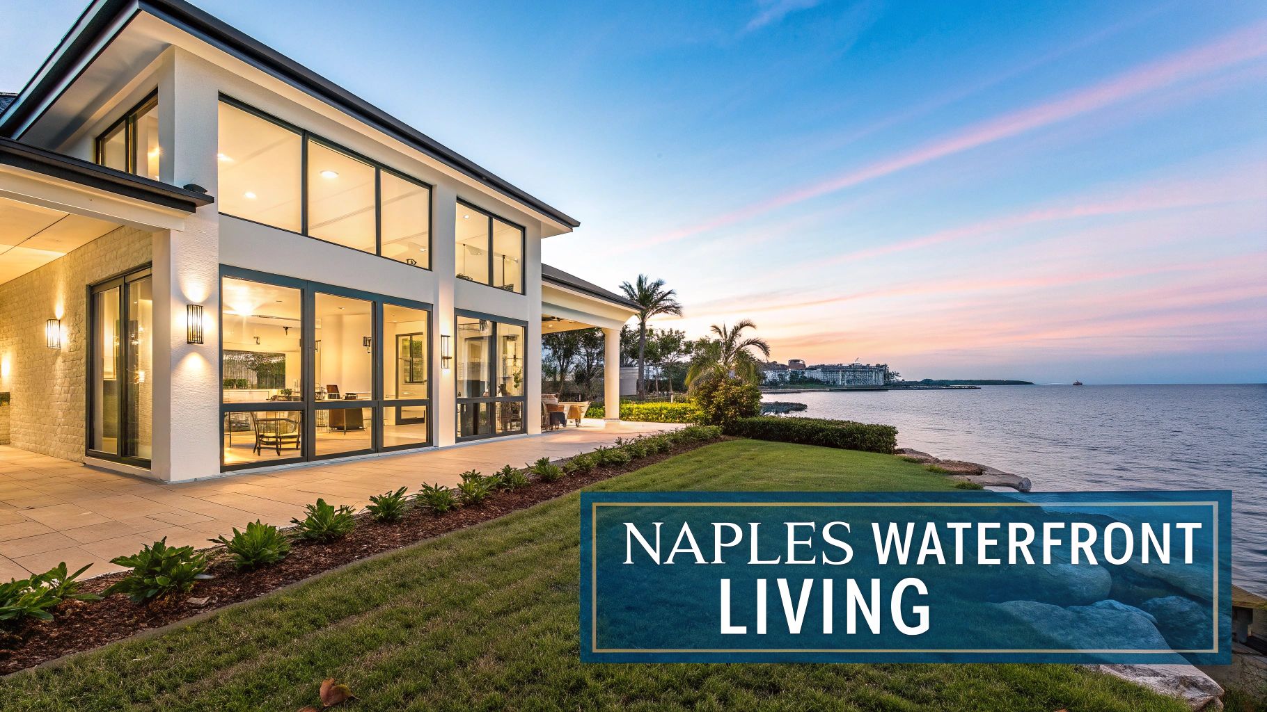 A modern white waterfront home with large windows and illuminated interior, set against a colorful sunset sky.