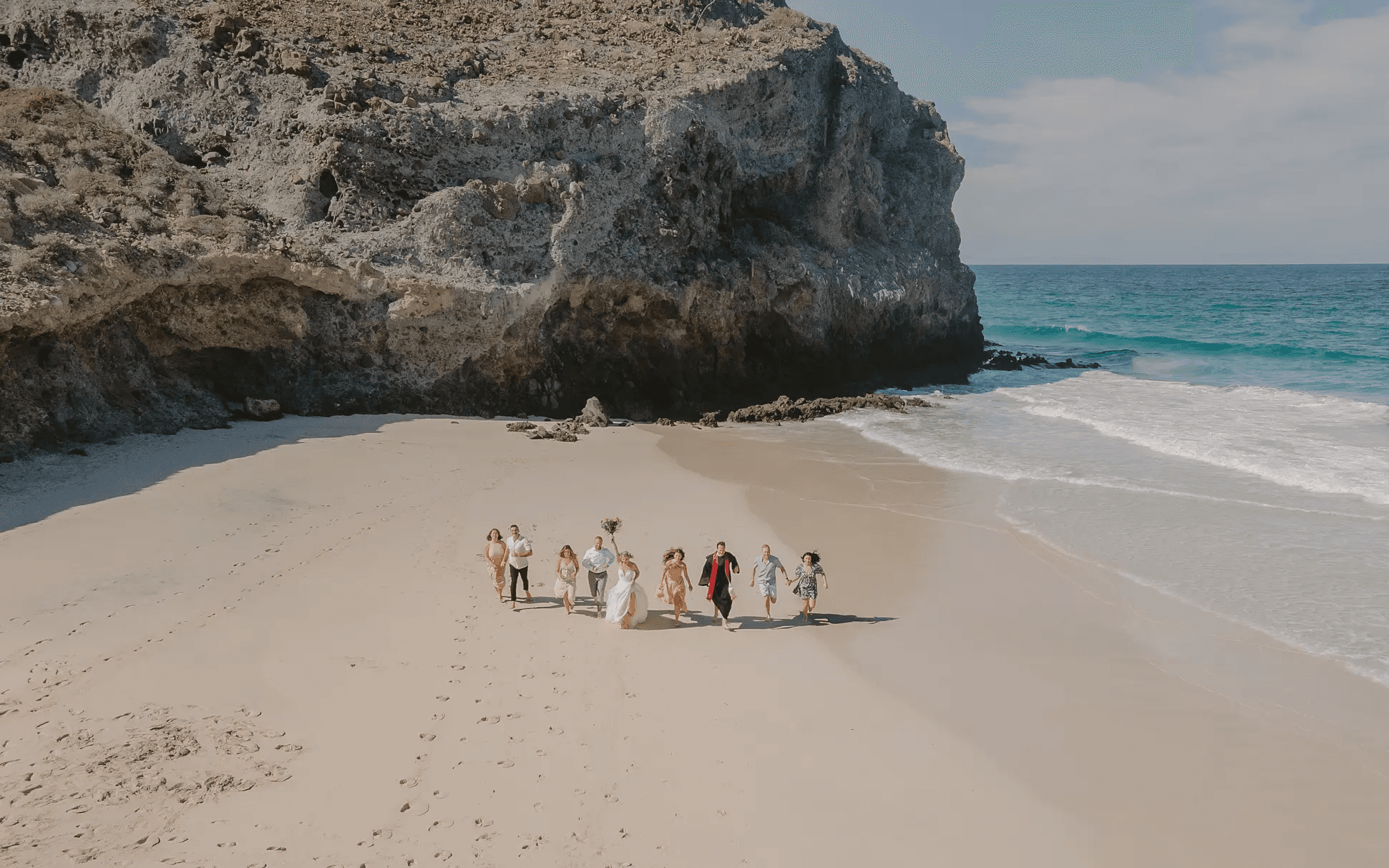 Wedding party walking on a beach beside a rocky cliff