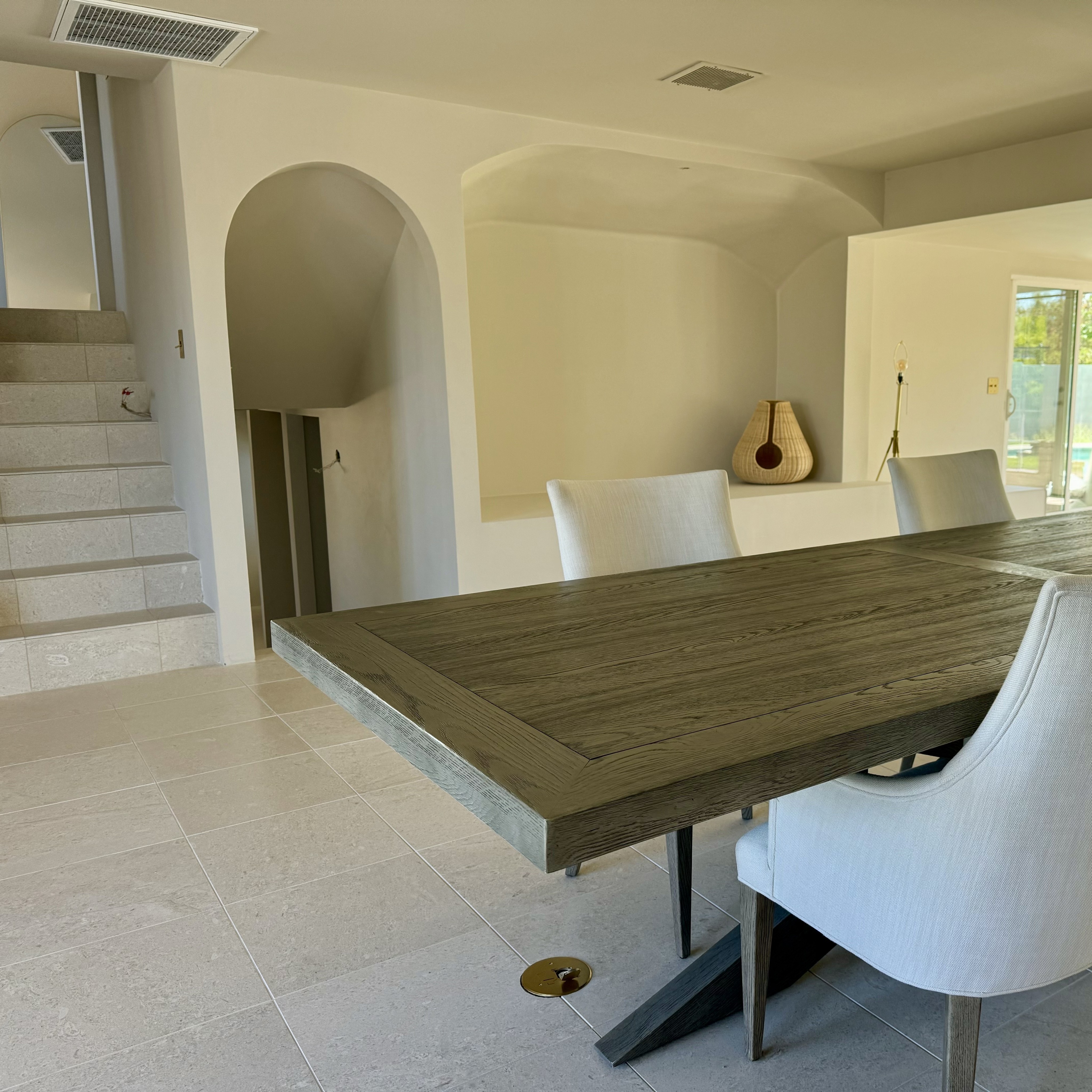 Modern dining area with marble tile flooring, wooden dining table, white chairs, and arched alcove in a new home.