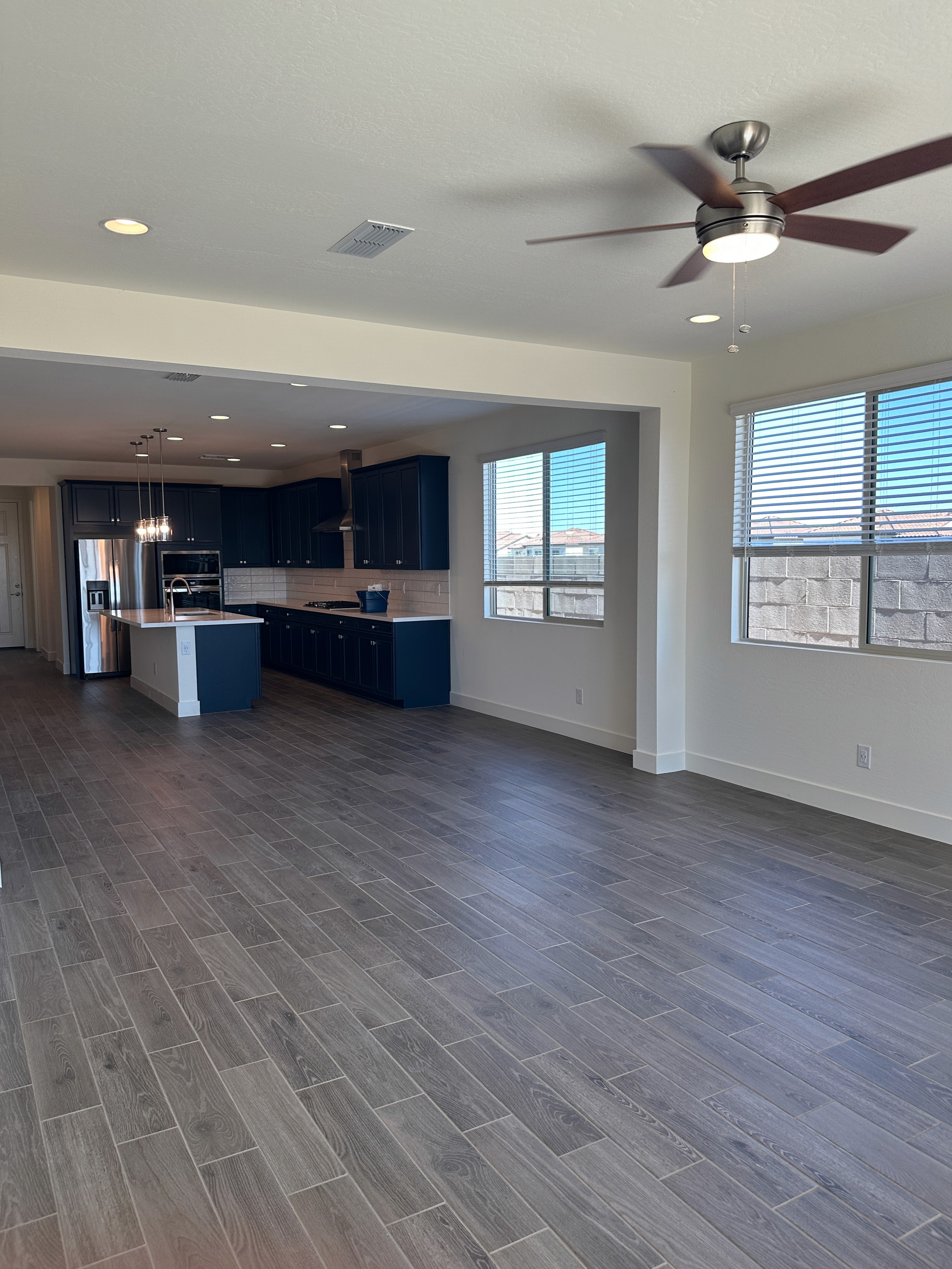 Modern open-plan kitchen and living area with dark cabinets, wood-look tiles, and a ceiling fan during construction.