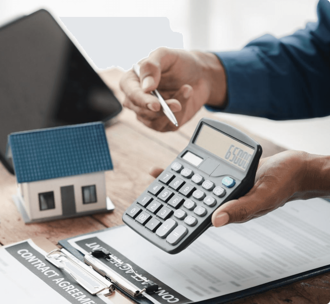 Person using a calculator next to a model house and contract agreement for financial planning and homeownership.