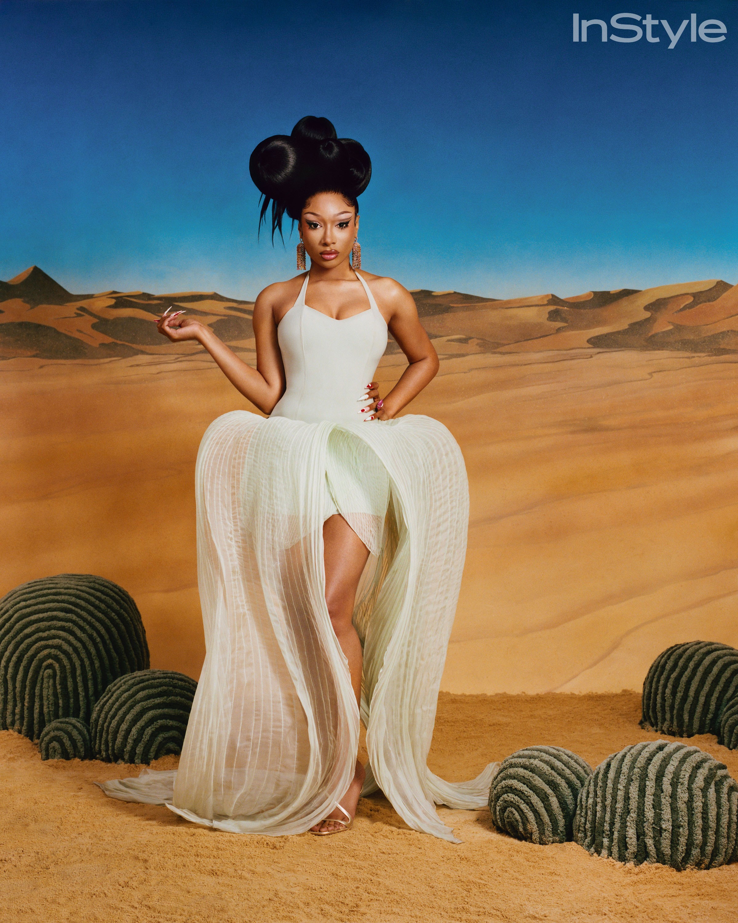 Megan Thee Stallion standing in a flowing white dress among sculptural cacti