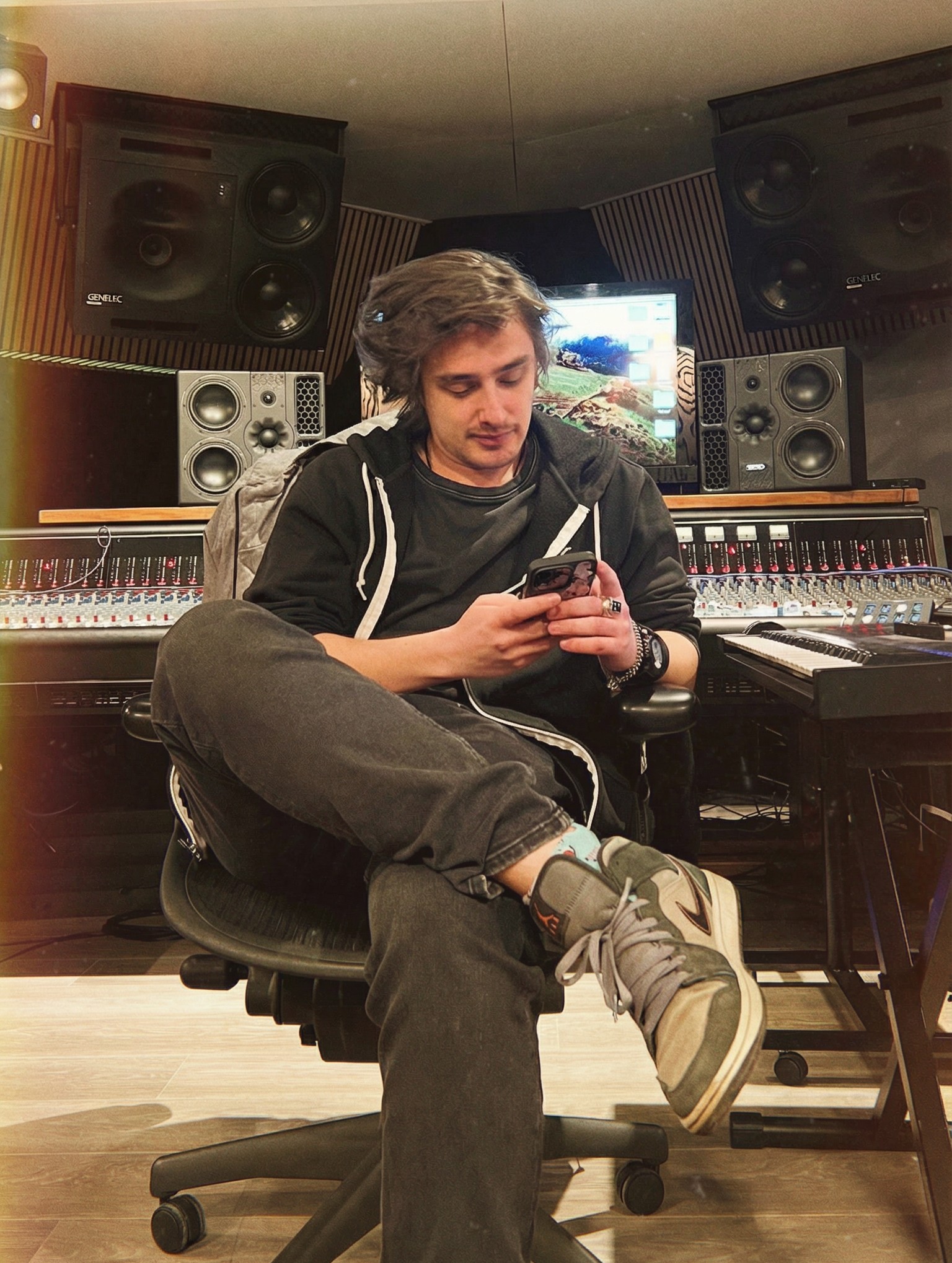 LeShaman sitting in a recording studio, checking his phone with studio monitors and mixing desk behind him.