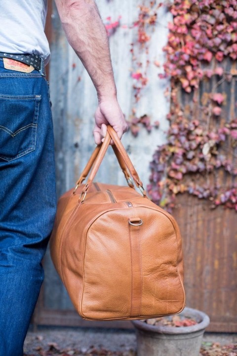 A smiling young man with crossed arms, wearing a plaid shirt and white t-shirt, poses against a dark background.
