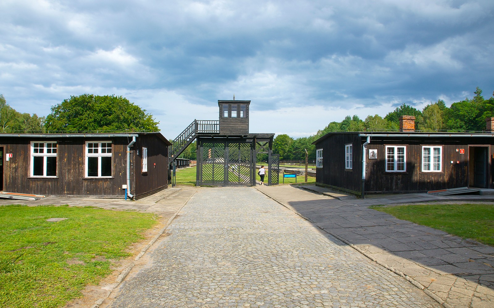 Wejście do obozu koncentracyjnego Stutthof z drewnianymi budynkami i wieżą wartowniczą.