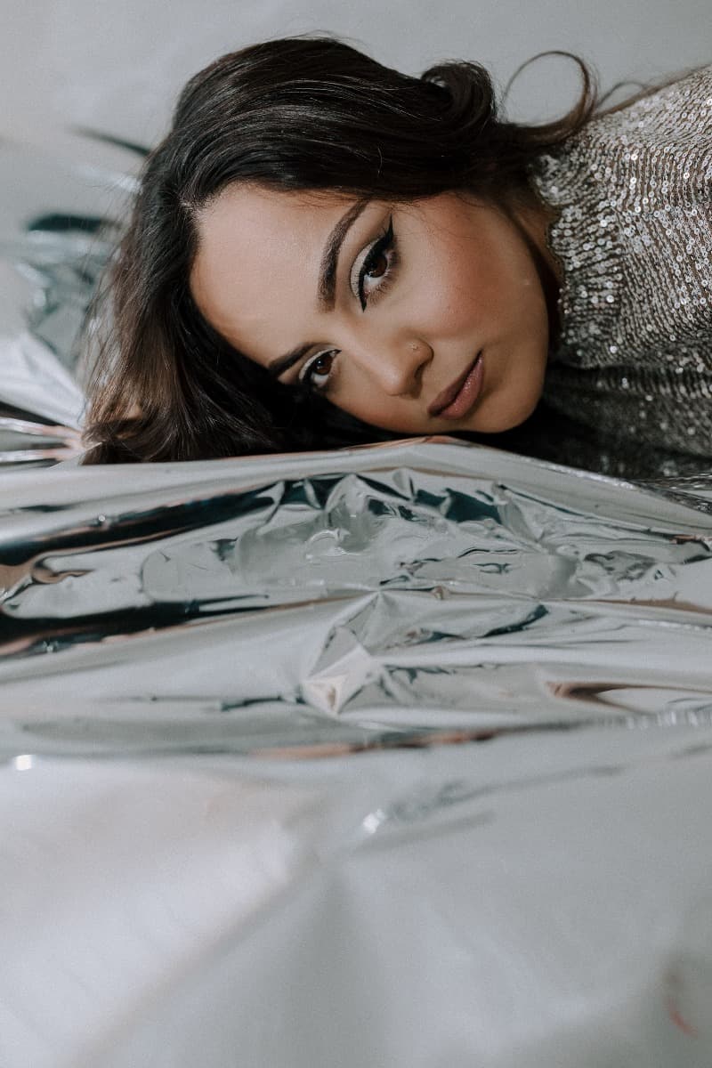 A close-up of a model lying on reflective Mylar, showcasing her makeup and metallic-themed styling during a creative shoot at Revelator Studio, Shreveport.