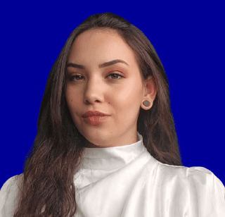 A smiling young man with crossed arms, wearing a plaid shirt and white t-shirt, poses against a dark background.