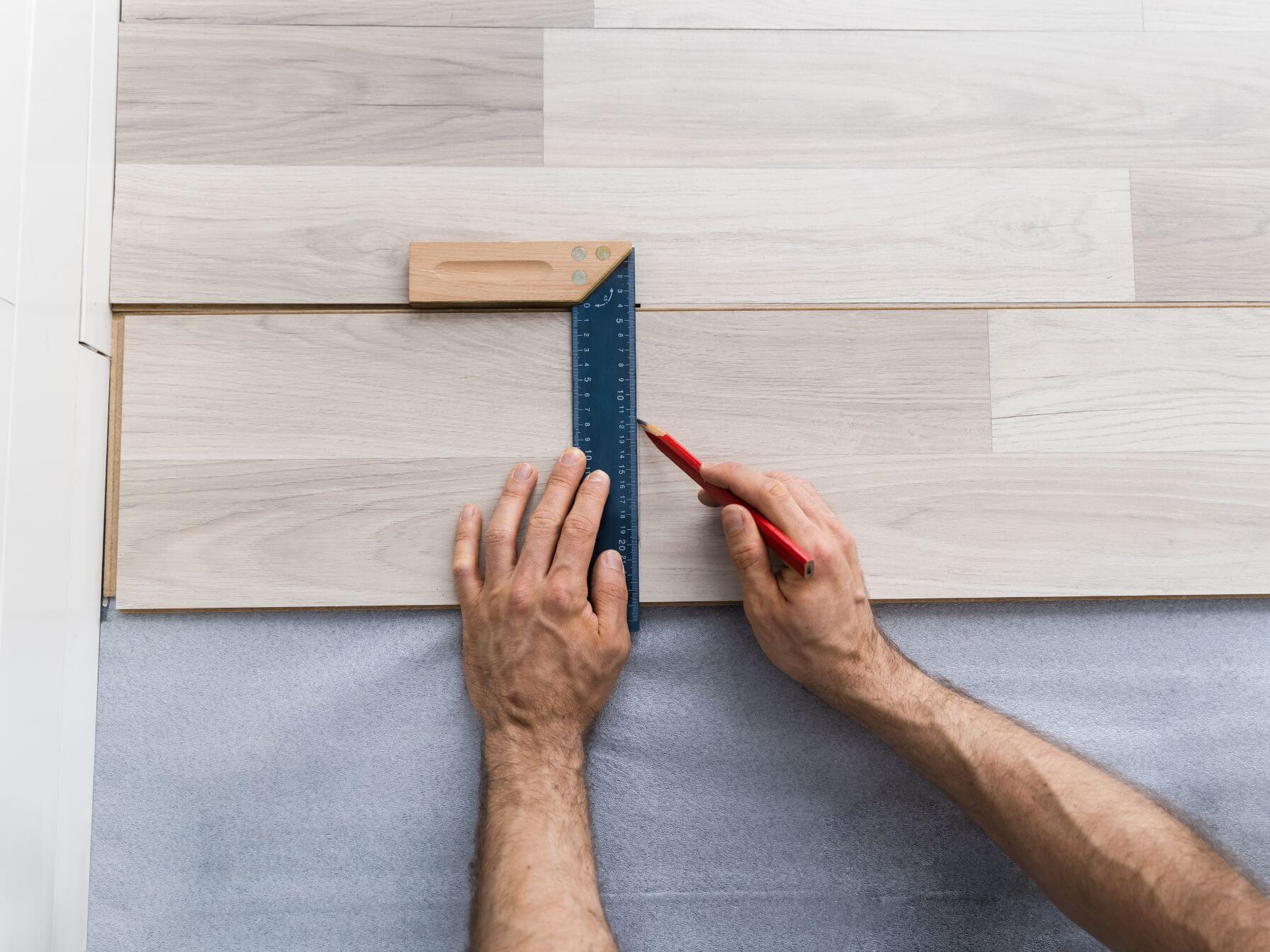 師傅精確量度及標記地板材料，展示專業木紋膠地板鋪設工藝，提供優質香港地板安裝及裝修工程服務。