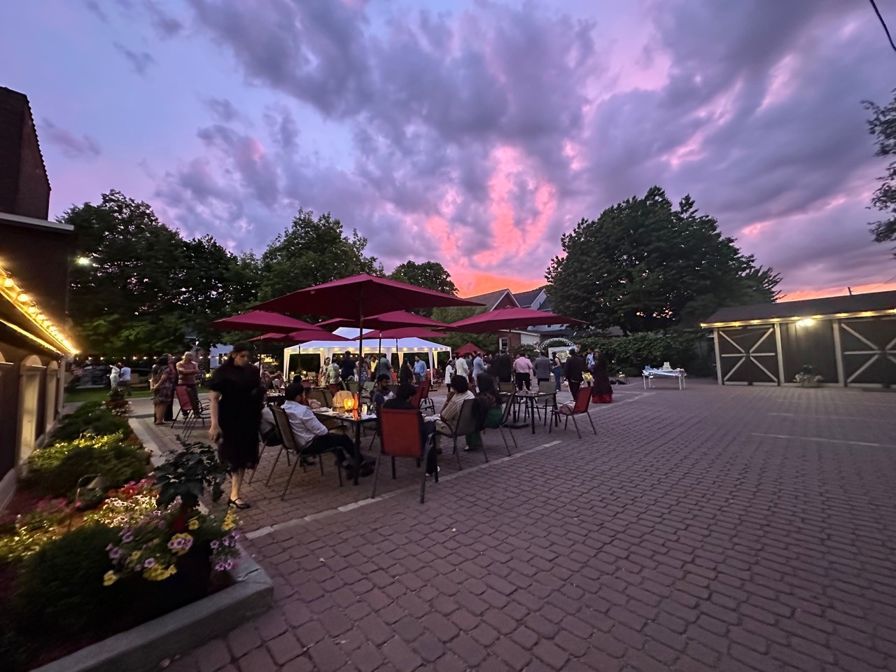Guests gathered in Bell Garden Courtyard at dusk with red umbrellas and courtyard lights.