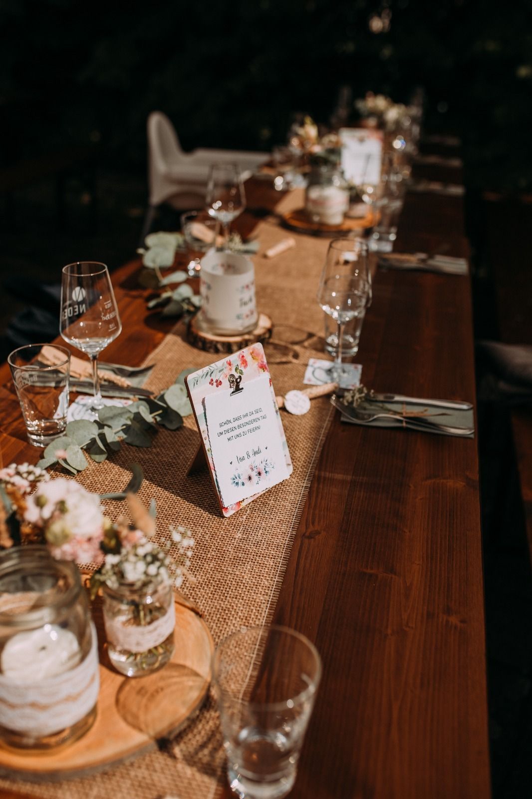 Hochzeits-Tischdeko auf Holztischen mit Eukalyptus, Menükarten und Weingläsern.