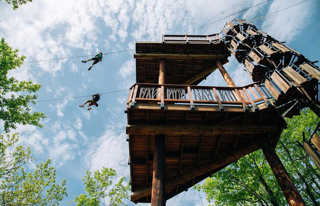 Two zipliners take off from a huge zipline platform with spiral staircase
