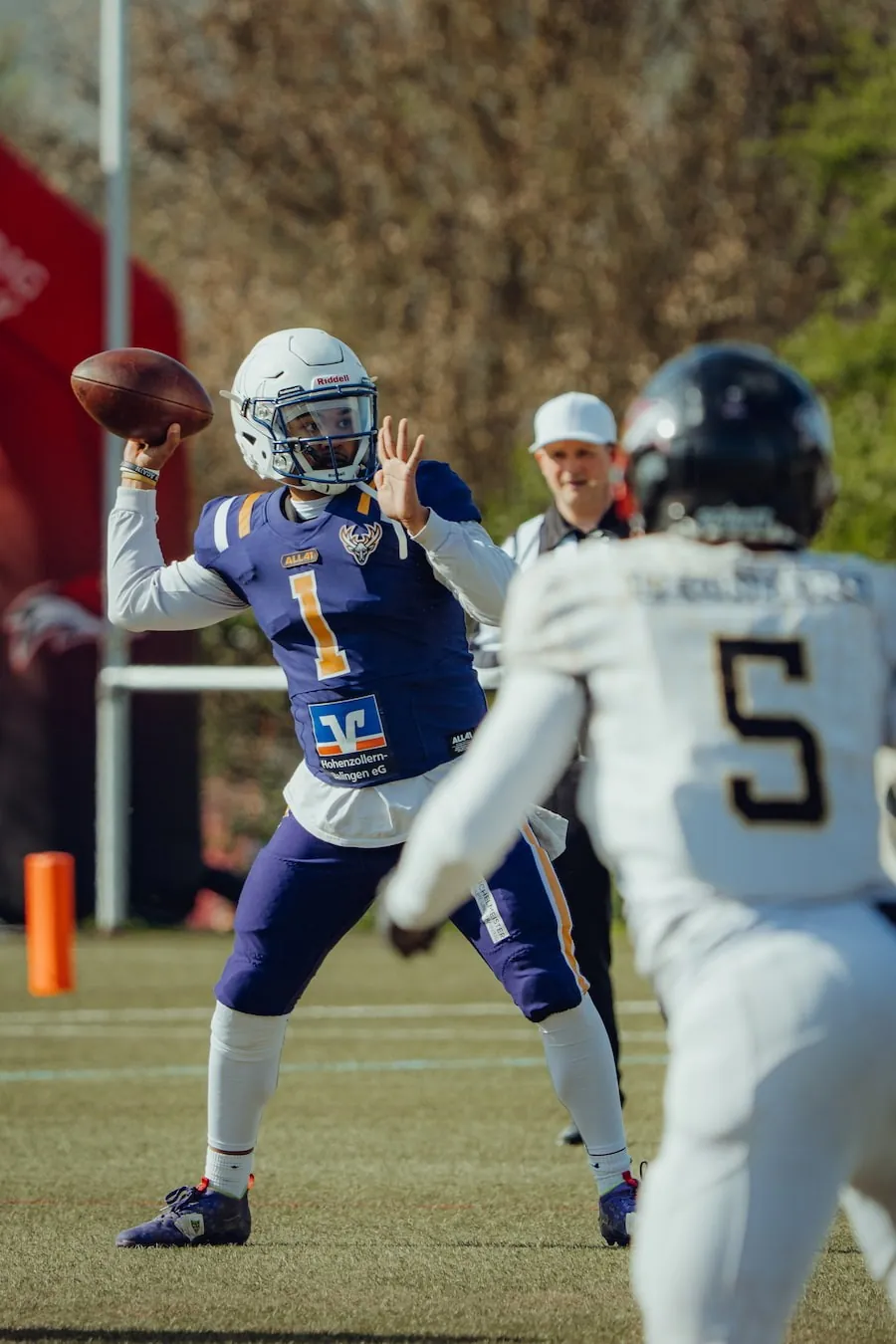 Der Quarterback der Bucks im blau-goldenen Trikot wirft den Ball, ein Gegner in Weiß stürmt heran.