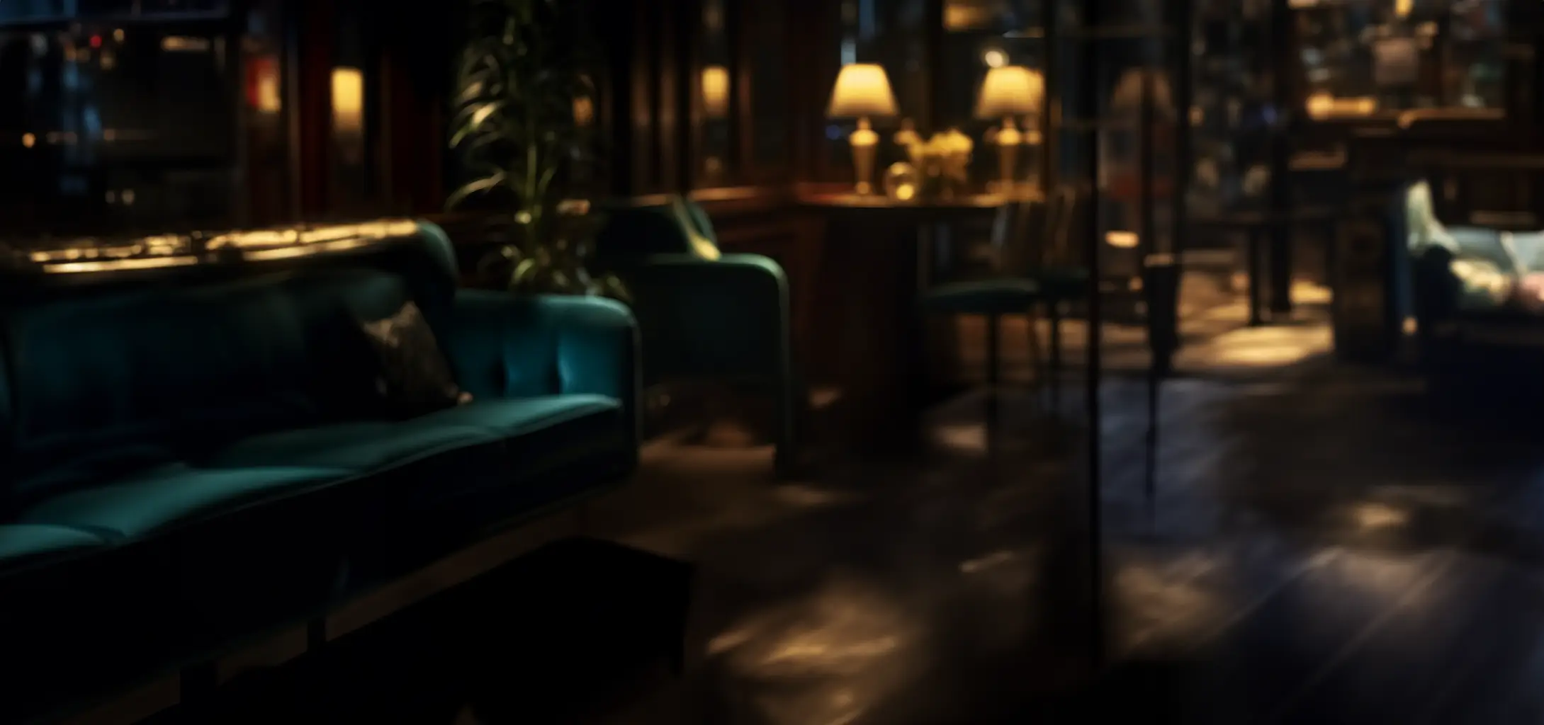 A dimly lit, cozy lounge features plush teal sofas, a few side tables with warm lamps, and a plant, creating an inviting atmosphere for relaxation.