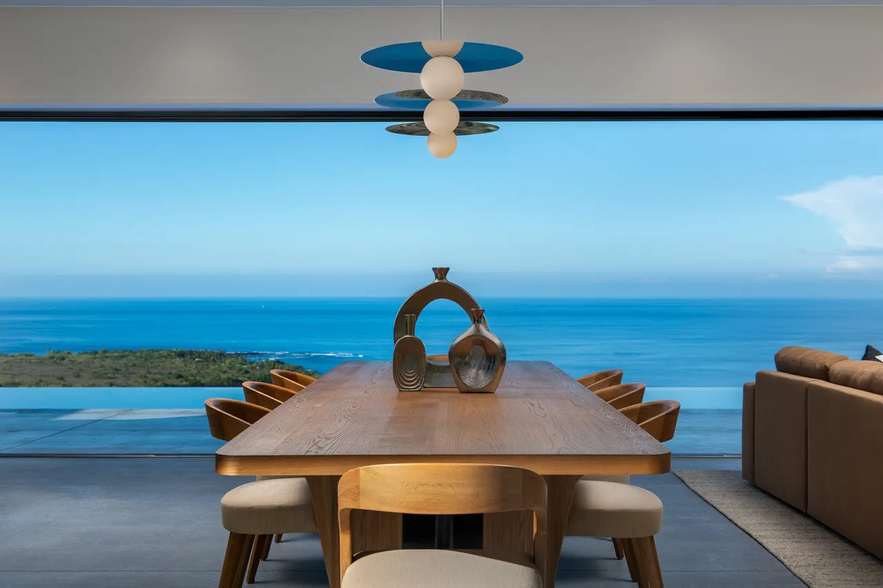 Dining table facing the ocean beneath a sculptural pendant, Nāpōʻopoʻo Hale
