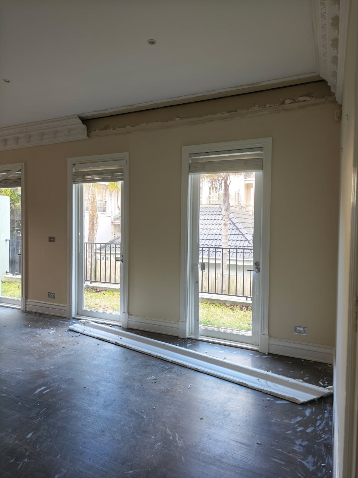 A modern hallway features vibrant teal and orange geometric and leaf patterns, with glossy tiled floors, a large rectangular light fixture, and a small shelf holding a potted plant, all leading to a large, frosted window at the end.