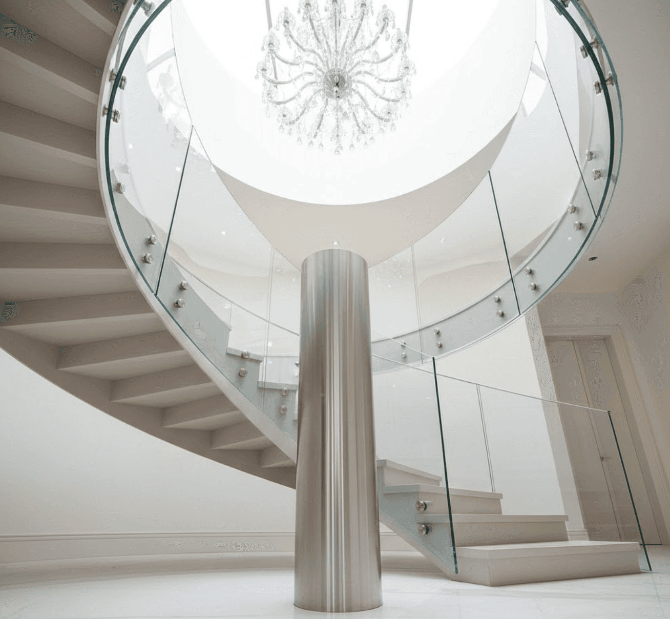 Elegant spiral staircase with curved glass balustrade following helical path. Polished stainless steel central column. White oak treads radiating from centre.