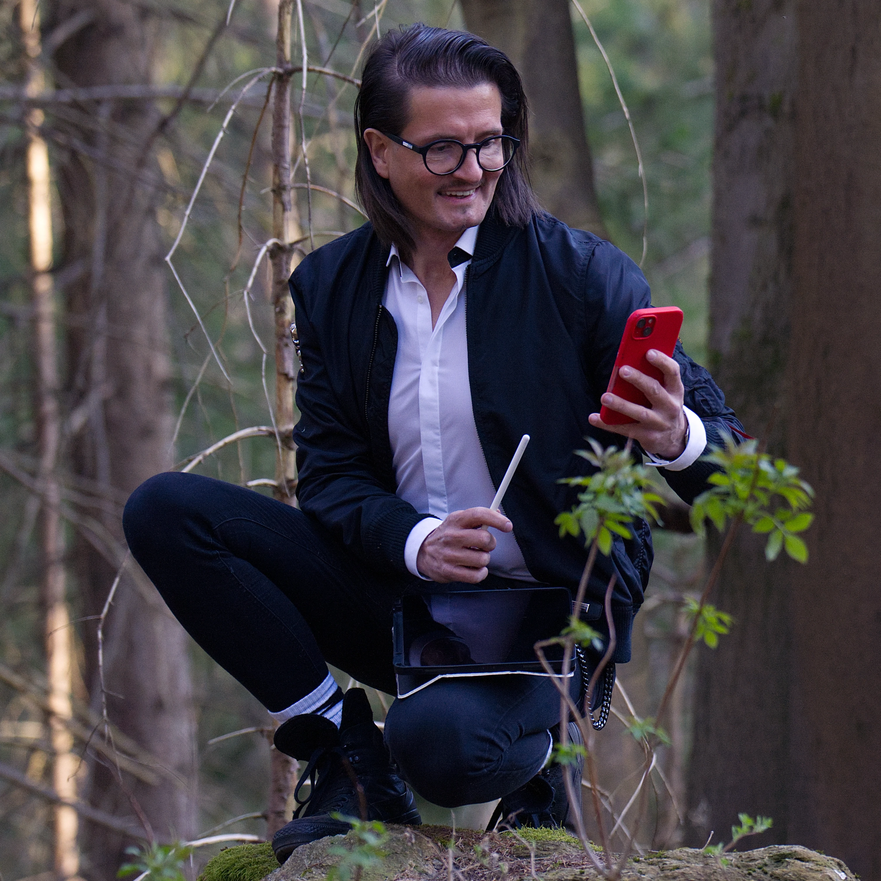 Man with short hair and beard wearing a dark blazer and black shirt against a plain background.