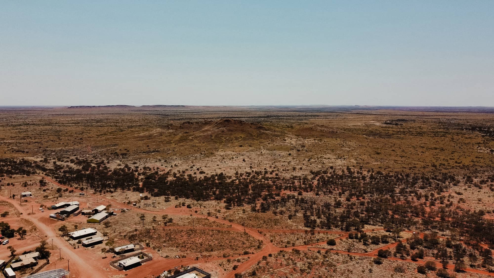 Aerial view of a remote industrial site in the Pilbara region of Australia with arid landscape and scattered buildings.
