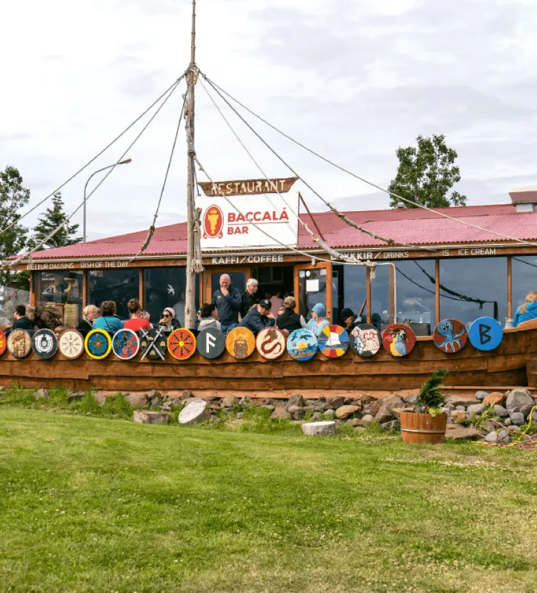 Exterior view of a coastal restaurant with colorful Viking shields decoration on a green lawn.